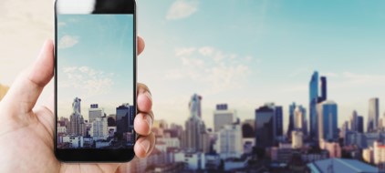 Mans hand holding mobile device with city in background and on screen