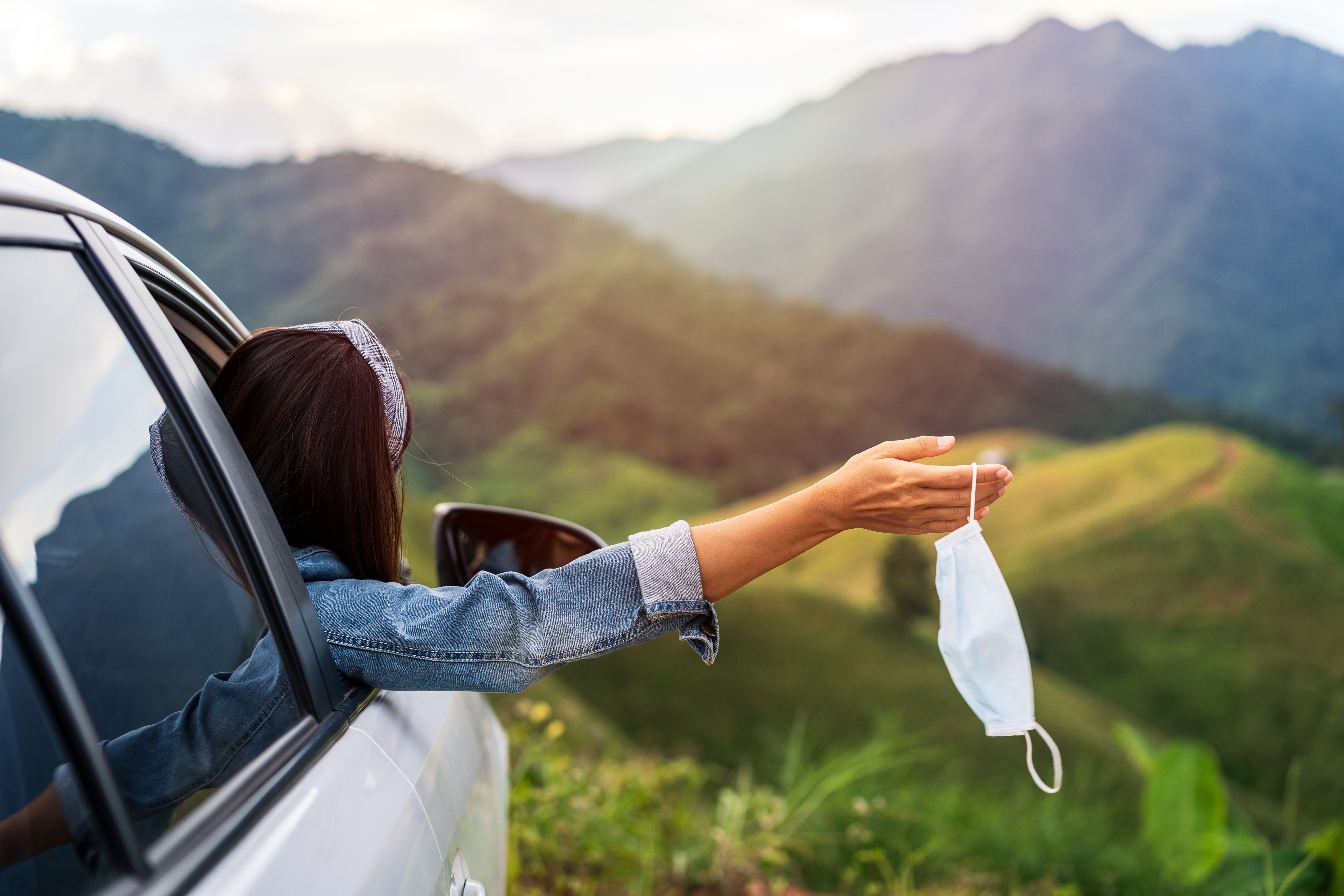 Young woman traveler taking off surgucal mask and looking beautiful mountain view while travel driving road trip on vacation
